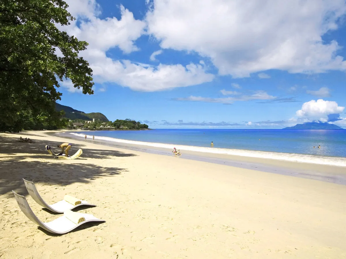 Pogled na peščeno plažo Beau Vallon z ležalniki pod palmami Berjaya Beau Vallon Bay Resort & Casino