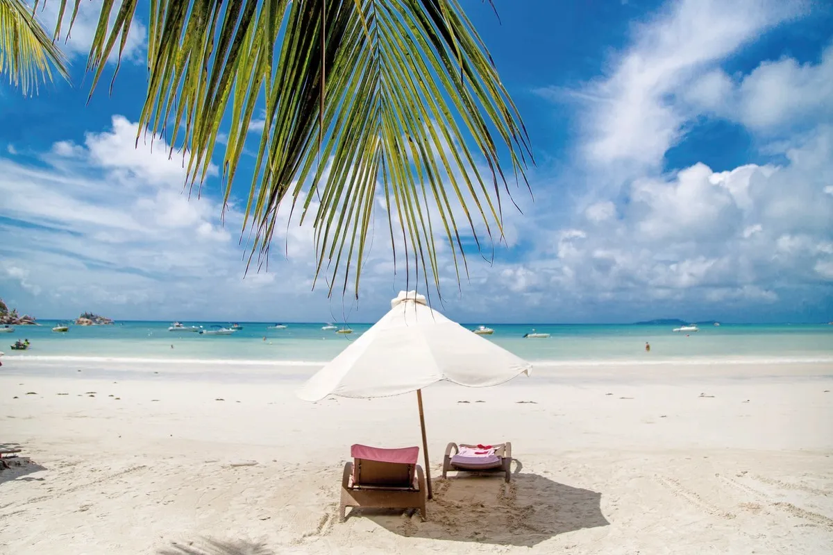 Pogled na tirkizno morje in belo mivko s senčnikom